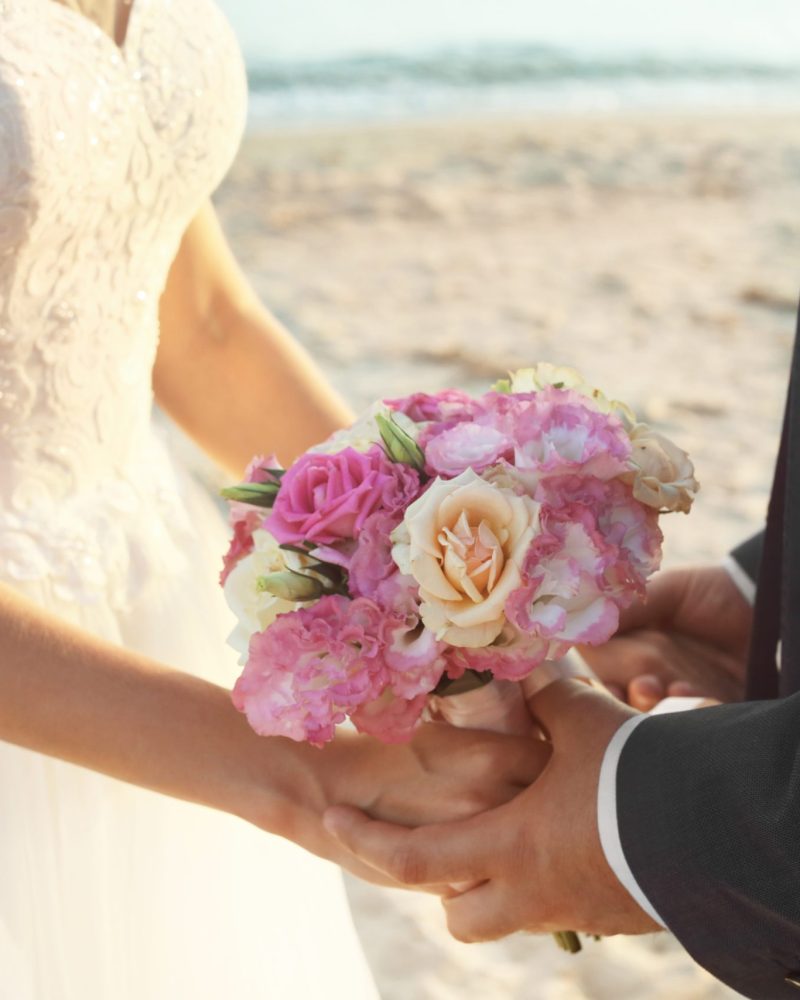 Close up view of wedding couple holding bouquet on beach