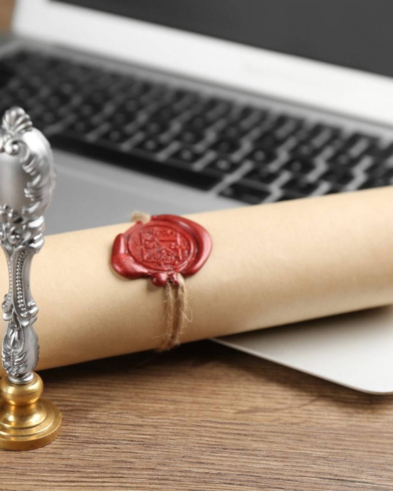 Notary's public pen and sealed document near laptop on wooden table