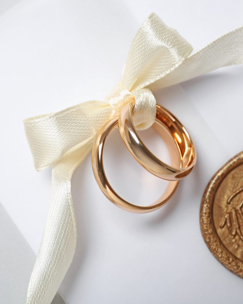 Wedding rings tied with ribbon and love letter on light background, top view